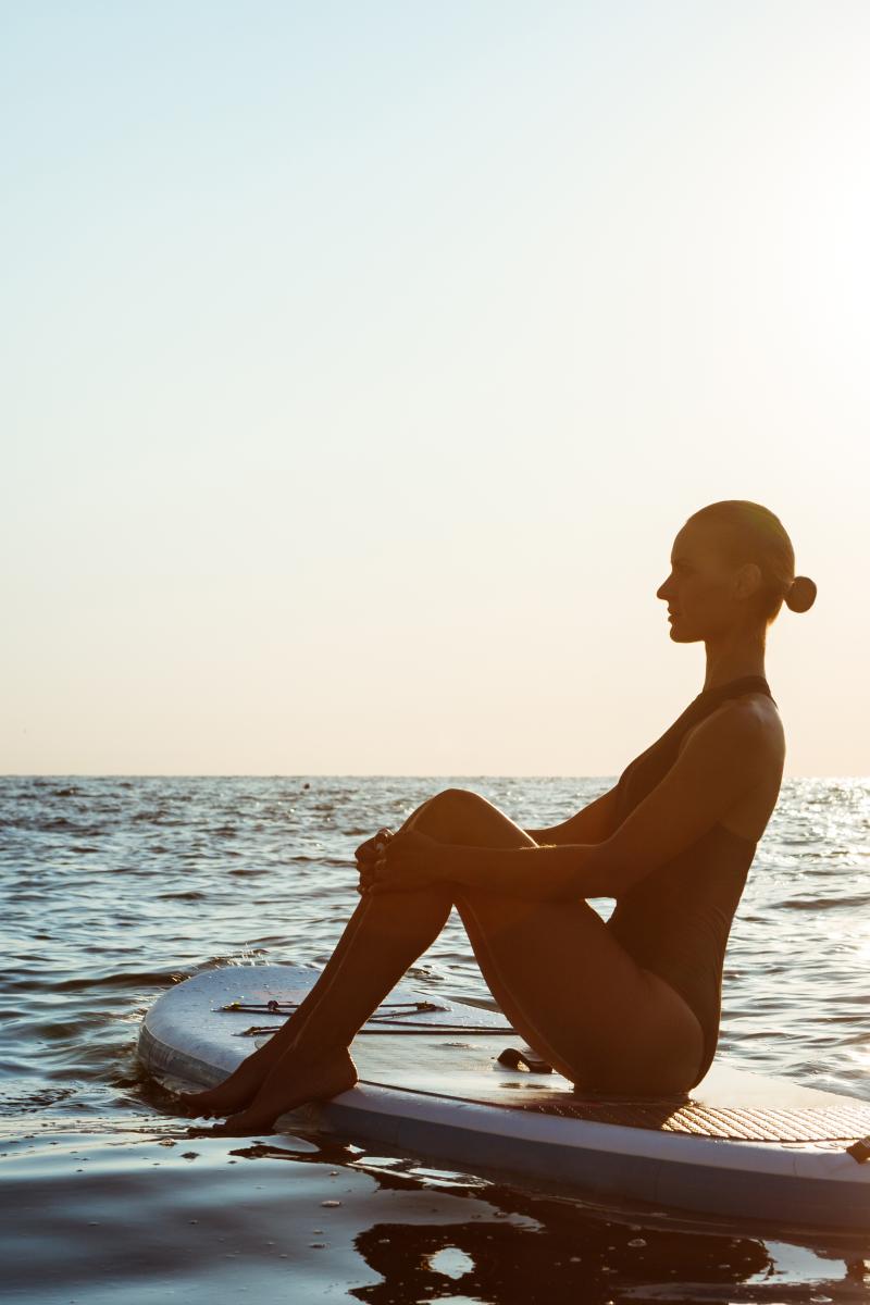 woman-practicing-yoga-surfboard-sunrise
